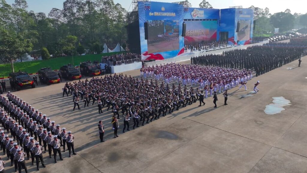 Presidenri go id010720261322556a44b23f2120d6 88678411e1782887002294 catrawarta Large outdoor parade with many uniformed groups marching in formation a blue stage and screens in the background and parked armored vehicles on the left